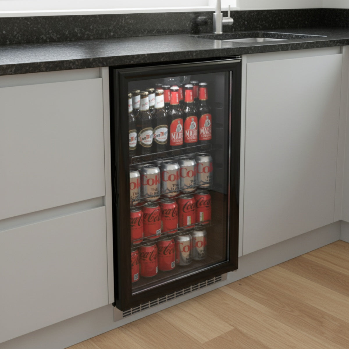 Under counter view of the Prodis beverage cooler positioned beside a kitchen sink, showing compact fit and clear glass display of bottled drinks