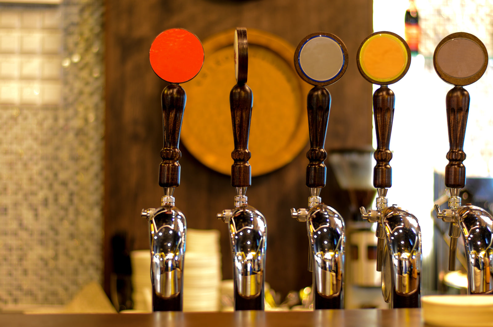 Row of traditional beer hand pulls with dark wooden handles and chrome spouts on a bar counter in warm pub setting.